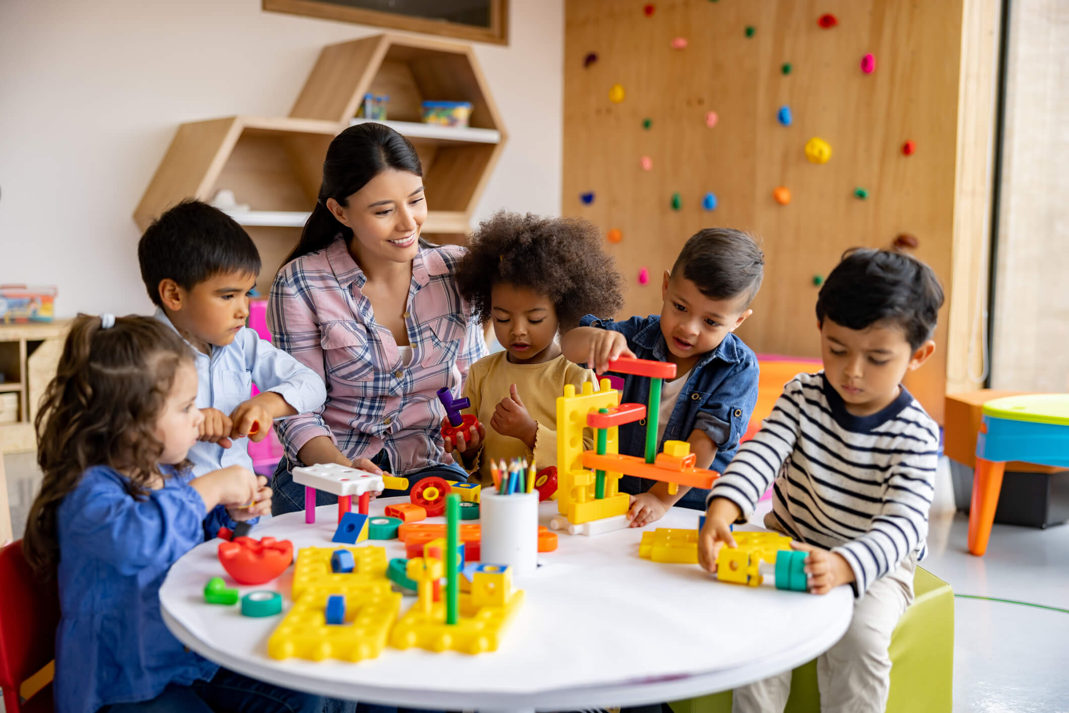 A teacher and group of preschool students playing with blocks at a table