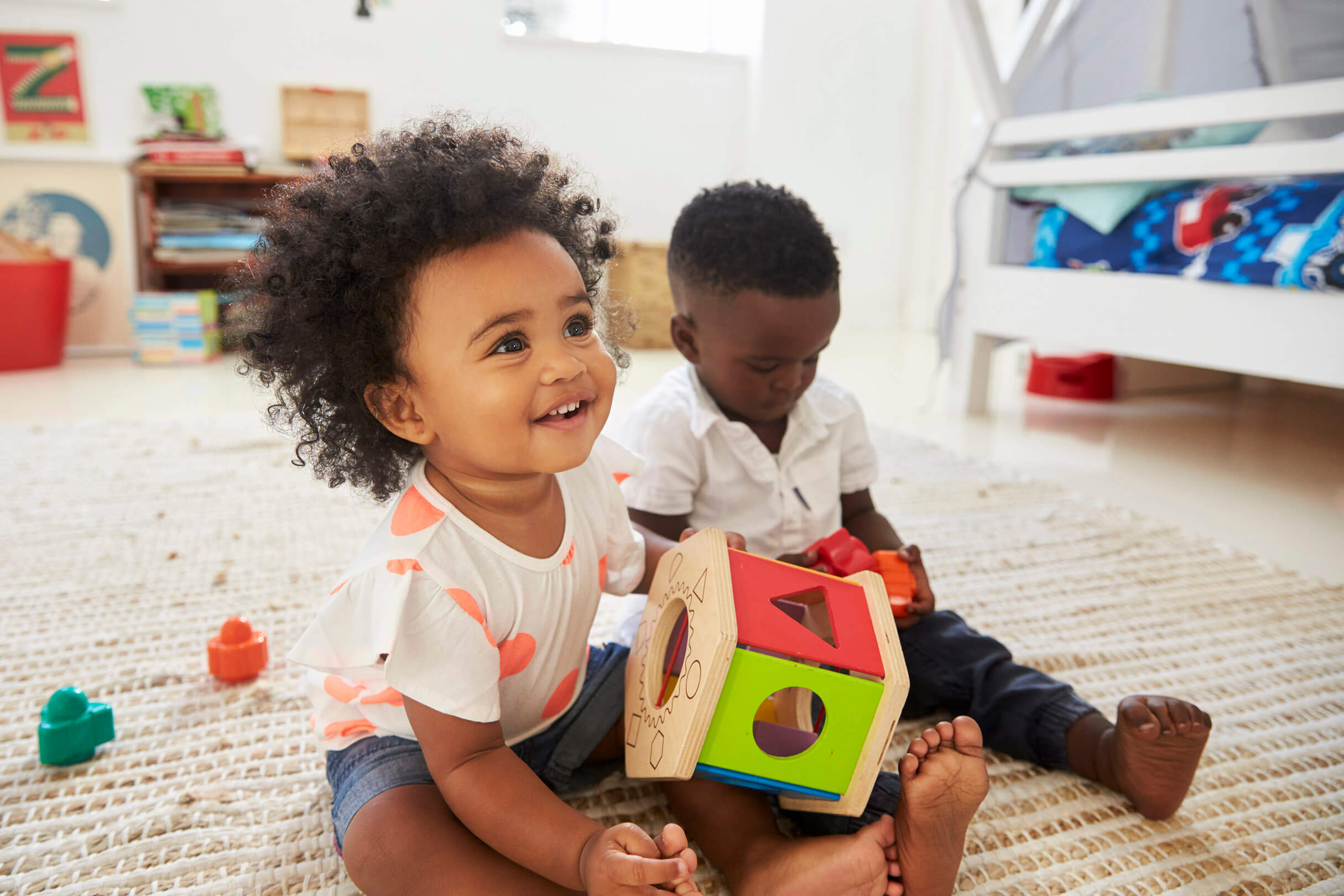 A child sitting on the floor playing with her child care provider